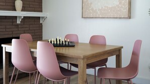 A dining area with a wooden table, pink chairs, a chessboard, a fireplace, and a framed artwork on the wall. - 4bd & Sleeps up to 10 - Saltwater Pool, Sunloungers, Mini Golf & Game Room (Indio)