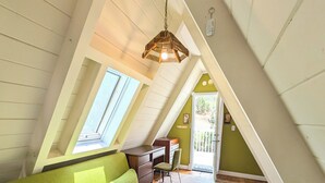 A cozy attic bedroom with a green sofa, a wooden desk, and a patterned rug. - Cozy 1960s A- Frame with Mountain Views (Bodfish)