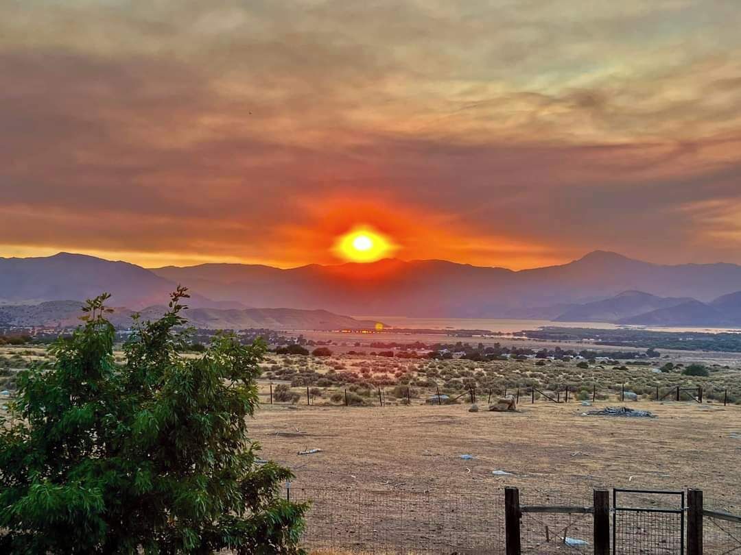 A sunset over a mountainous landscape with a fenced area in the foreground.