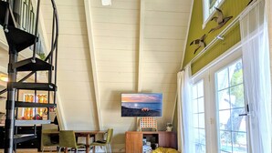 A spacious living room with a high ceiling, a spiral staircase, a flat-screen TV, and large windows. - Cozy 1960s A- Frame with Mountain Views (Bodfish)