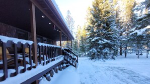 Una cabaña de madera con un porche cubierto y una terraza cubierta de nieve.