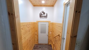 Un interior de madera con una puerta al final, un cartel de bienvenida con un alce y una rejilla metálica en el suelo.