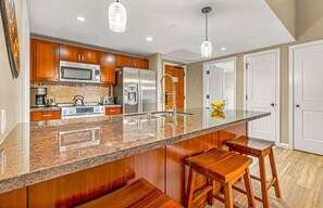 A modern kitchen with wooden cabinets, stainless steel appliances, a granite countertop, and bar stools.