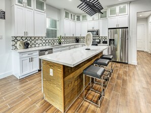 Une cuisine moderne avec des meubles blancs, un grand îlot central doté de tabourets, un réfrigérateur en acier inoxydable et un pare-feu décoratif.