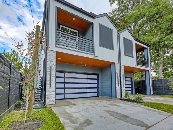 Une maison moderne à deux étages, dotée d’un garage, d’un balcon et d’une façade en pierre.