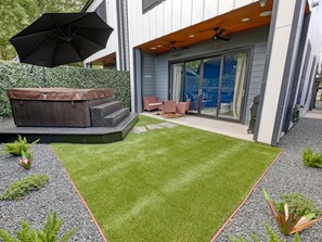 Une terrasse extérieure moderne, dotée d’un jacuzzi, d’un espace salon et d’une pelouse bien entretenue.