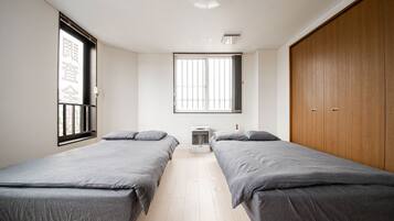 Una habitación con dos camas individuales, una ventana con rejas, un armario de madera y una lámpara en el techo.