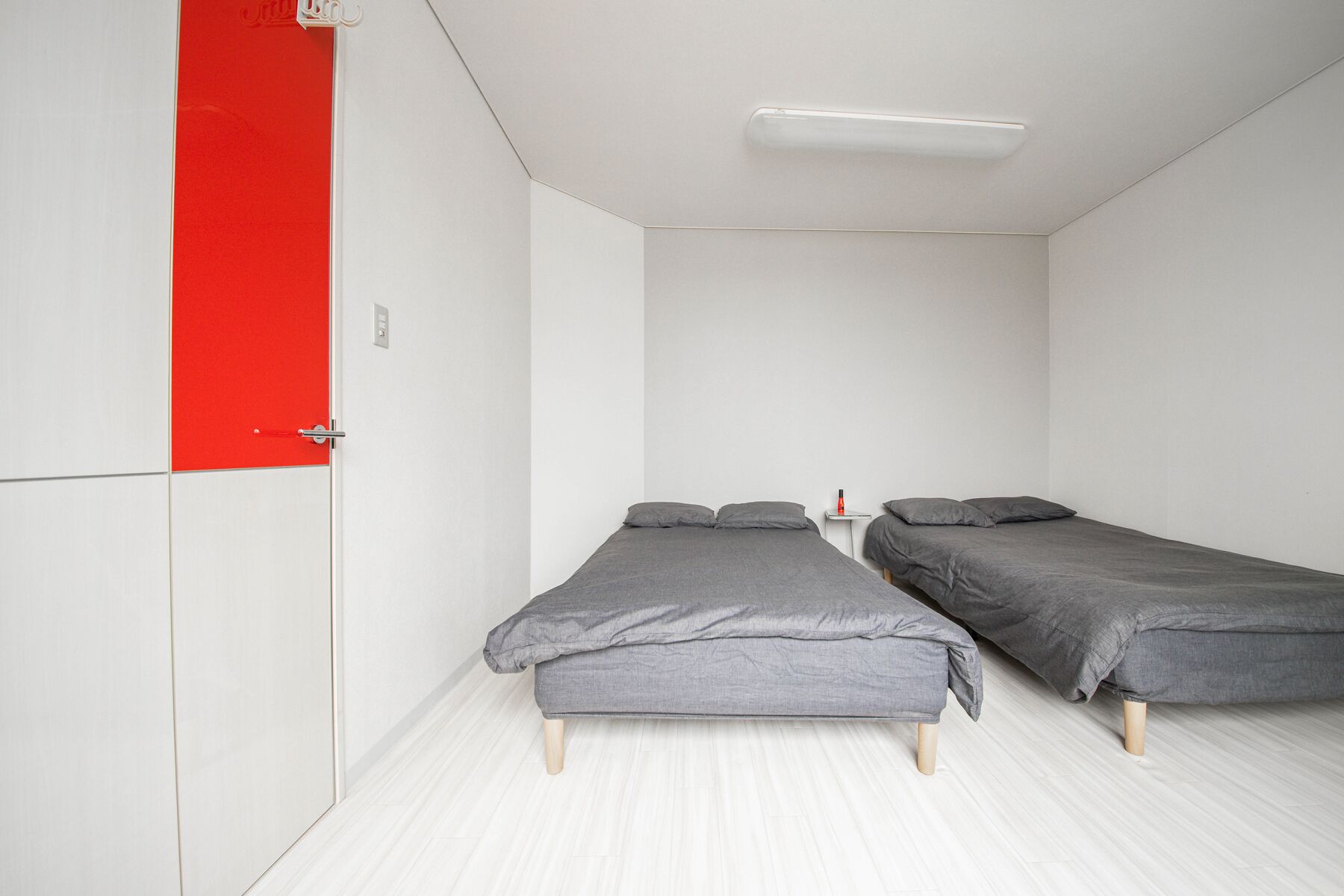 A room with two single beds, a red door, white walls, and a light-colored floor.