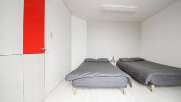 A room with two single beds, a red door, white walls, and a light-colored floor.