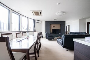 A modern living room with a large flat-screen TV, a dark-colored sofa, and a dining area with a glass table and chairs. - ROADSIDE HOUSE (Sapporo)