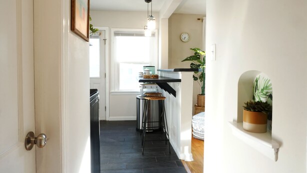 A narrow hallway with a kitchen area at the end, featuring a stove, sink, and stools.