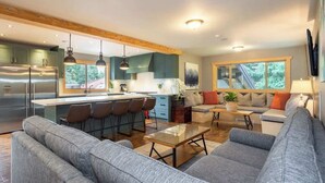 A modern kitchen with a central island, bar stools, and a dining area with a sofa and coffee table. - Whistler lodge with hot tub & cinema (Whistler)