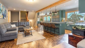 A modern living room with a gray sectional sofa, a wooden coffee table, and a bar area with stools. - Whistler lodge with hot tub & cinema (Whistler)