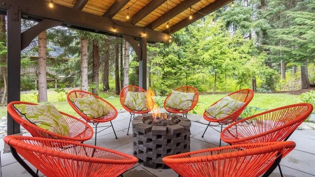 A covered outdoor seating area with a fire pit and red wicker chairs. - Whistler lodge with hot tub & cinema (Whistler)