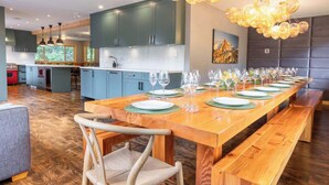 A modern kitchen with a long wooden dining table set for a meal, featuring a unique chandelier and a view of the outdoors. - Whistler lodge with hot tub & cinema (Whistler)