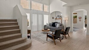 A spacious living room with a staircase, a gray sofa, and a coffee table. - The Agave Cowboy | 2 Car Garage | Community Pool (Phoenix)