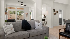 A modern living room with a grey sofa, a black leather chair, and a dining area with a table and chairs. - The Agave Cowboy | 2 Car Garage | Community Pool (Phoenix)