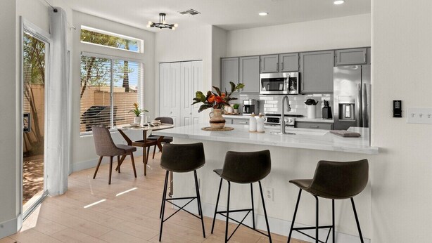 A modern kitchen with a central island, bar stools, and a dining area with a view of the outdoors. - The Agave Cowboy | 2 Car Garage | Community Pool (Phoenix)