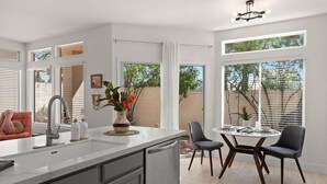 A modern kitchen with a central island, a dining area with a round table and chairs, and large windows providing natural light. - The Agave Cowboy | 2 Car Garage | Community Pool (Phoenix)