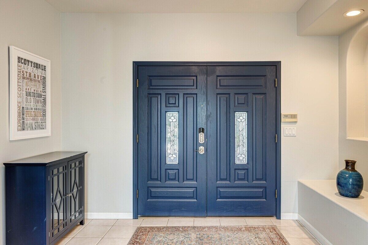 A dark blue double door with glass panels, a black console table, and a blue vase on a white shelf.