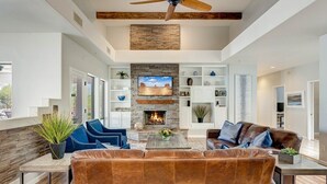 A spacious living room with a fireplace, leather sofas, and a ceiling fan. - Rancho Relaxo | 3 Acres + Casita + Pool (Scottsdale)