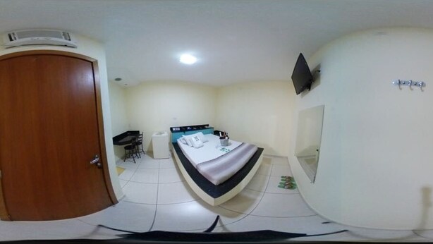 A compact hotel room with a bed, a desk, a chair, a wardrobe, and a television on the wall. - hotel e motel ape goiania anel viario (Goiânia)