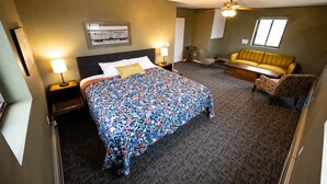 Quarto de hotel com uma cama grande, um sofá, uma cadeira, um ventilador de teto e uma janela.