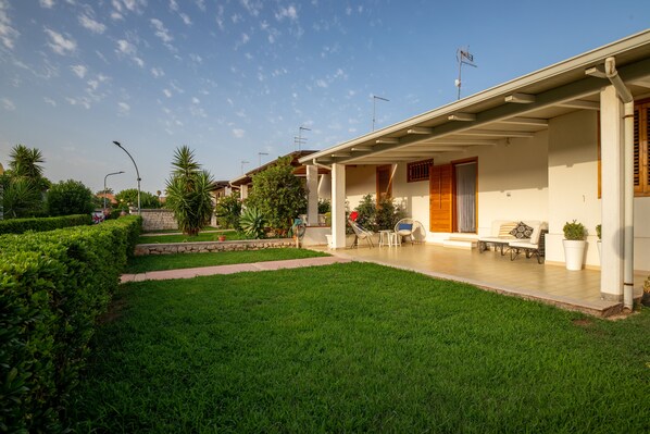 A residential property with a covered patio, a lawn, and a stone wall.