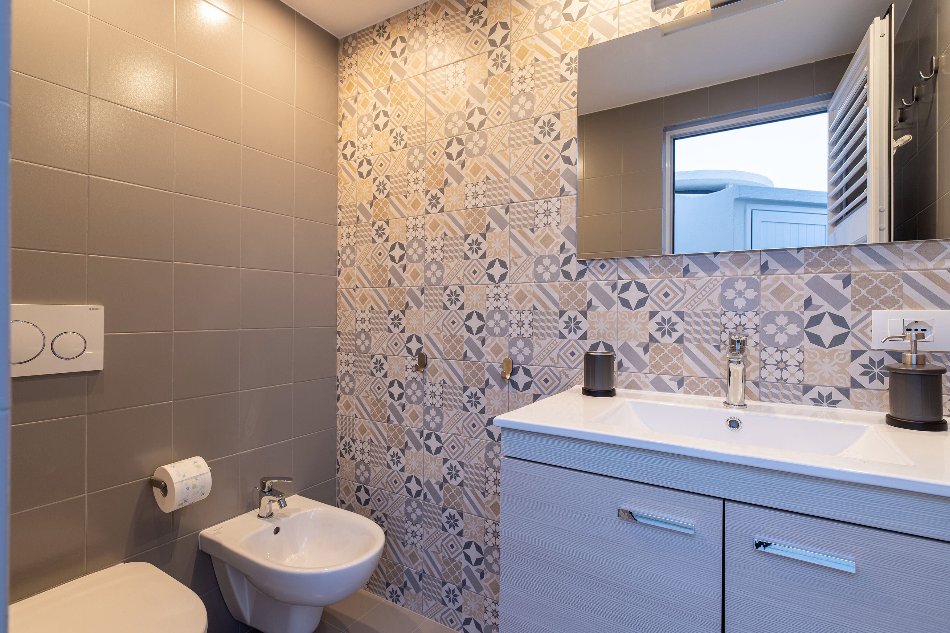 Ein Badezimmer mit einem Fliesenrückwand mit Muster, einem weißen Waschbecken und einem Bidet.