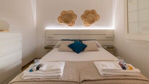 Ein ordentlich bezogenes Bett mit blauem Kopfkissen, weißen Laken und einer beigen Decke.
