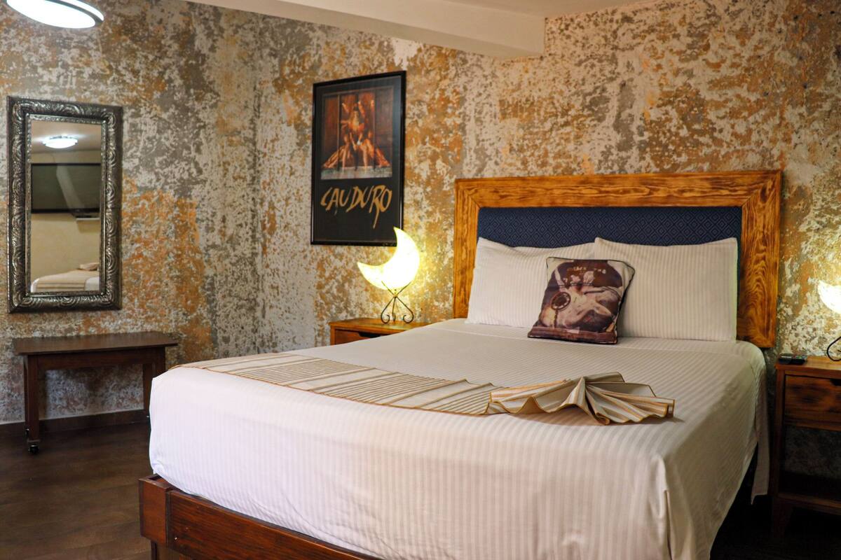 Un lit bien fait, avec une tête de lit en bois, un tableau encadré au mur et une table de chevet avec une lampe.