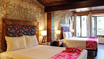 A room with two beds, each with a wooden headboard and a floral-patterned headboard. There are bedside tables with lamps and a window with curtains.