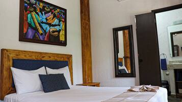 Una habitación de hotel con una cama grande, un cabecero de madera, un cuadro en la pared, un espejo y una puerta que da al baño.
