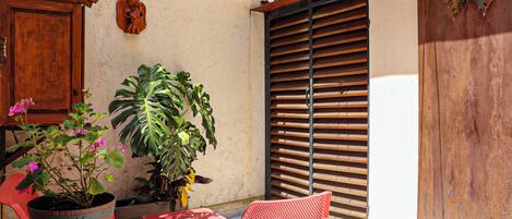 A patio with a wooden door, a potted plant, a red chair, and a table.