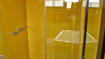 A bathroom with yellow walls, a white sink, a glass shower enclosure, and a mirror.