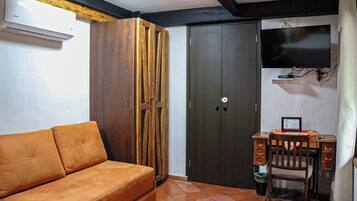A room with a sofa, a desk with a chair, a television, and a wardrobe.