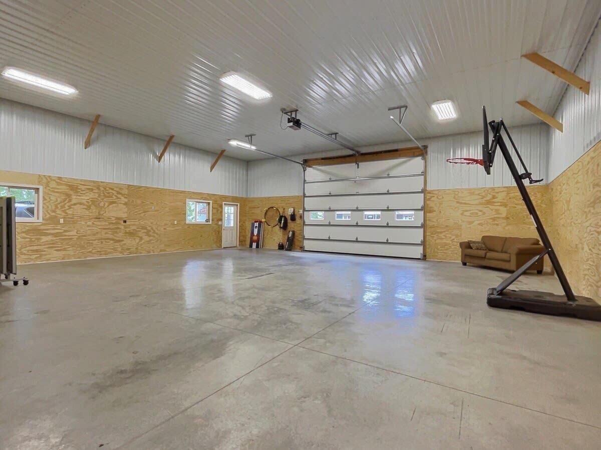 A spacious indoor area with a polished concrete floor, wooden panel walls, a large garage door, and a basketball hoop.