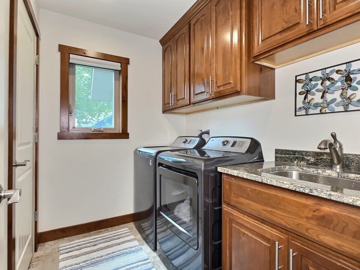 A laundry room with wooden cabinets, a washing machine, a dryer, a granite countertop, and a window.