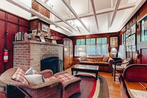 Cozy living room with a brick fireplace, comfortable seating, and a bookshelf filled with books and decorative items.