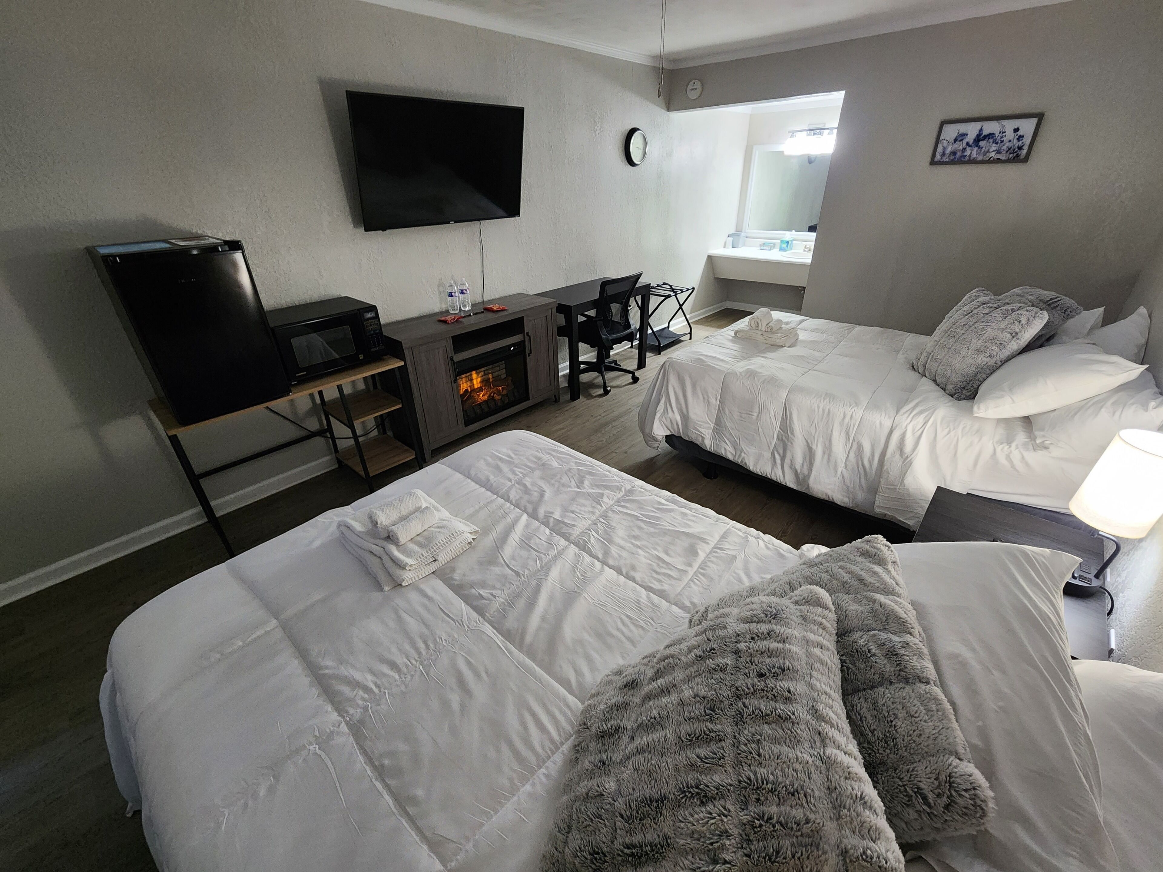 A hotel room with two beds, a flat-screen TV, a microwave, a small table with a fire feature, and a window with a view of the city.