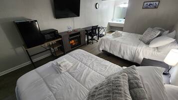 A hotel room with two beds, a flat-screen TV, a microwave, a small table with a fire feature, and a window with a view of the city.