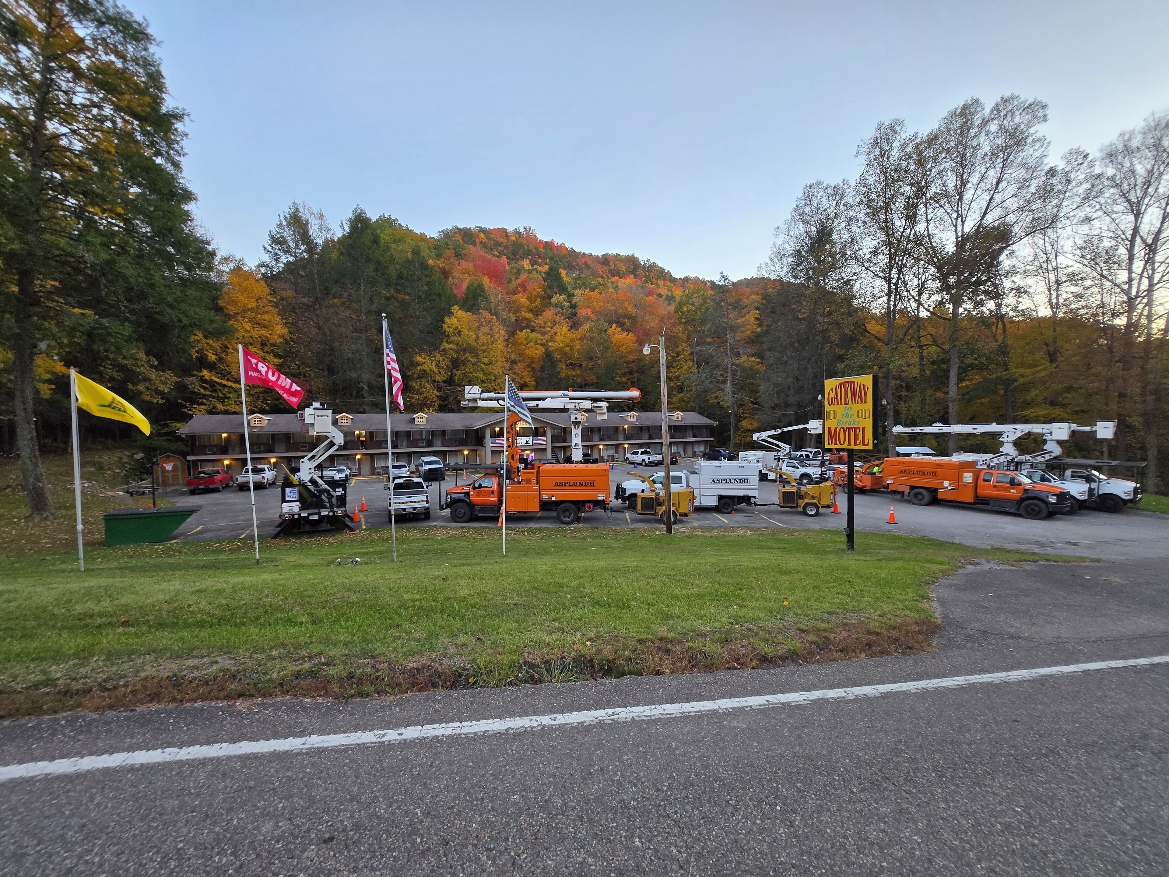 A motel with multiple utility vehicles and flags, surrounded by autumn-colored trees.