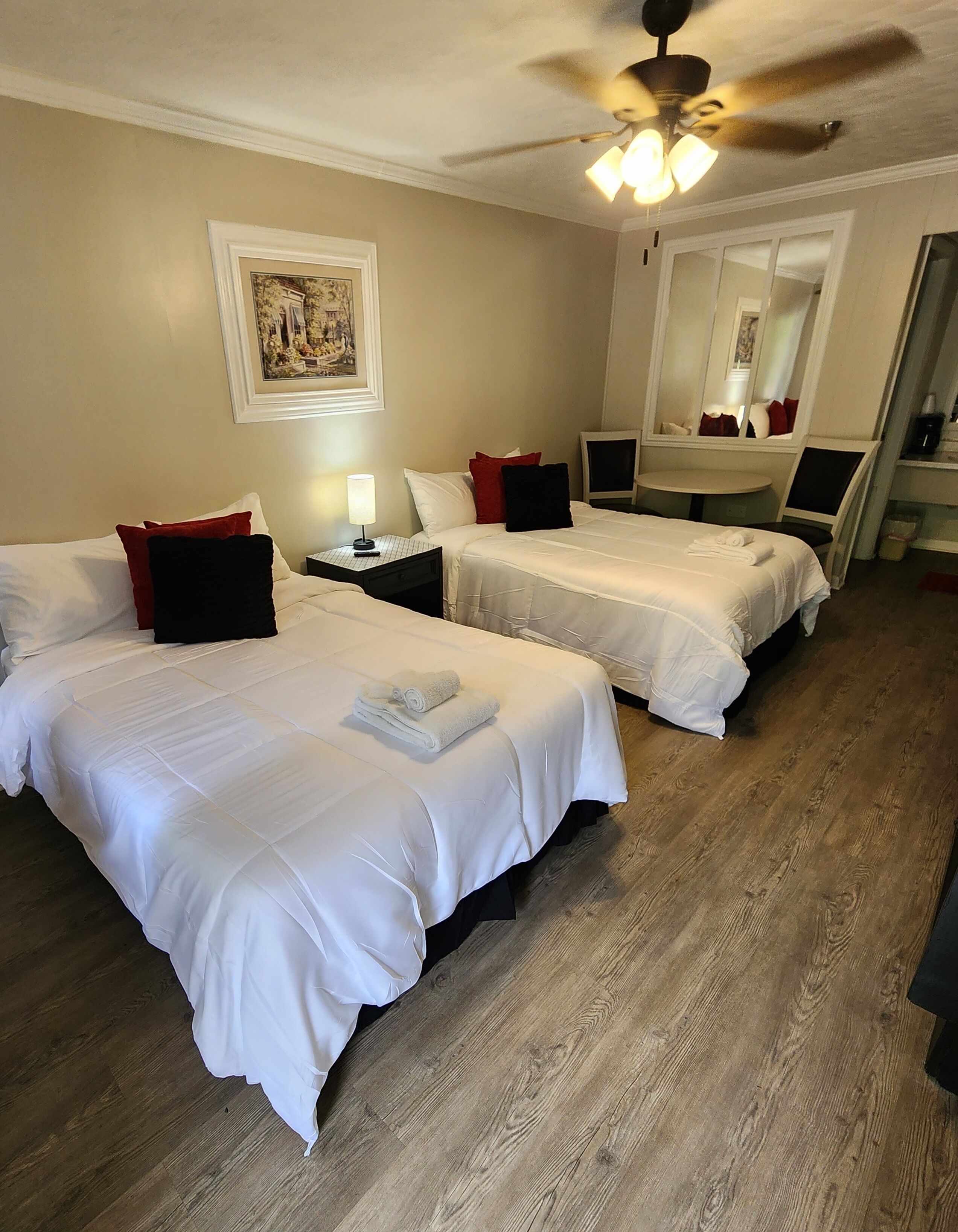 A hotel room with two beds, a round table, a ceiling fan, and a large mirror.