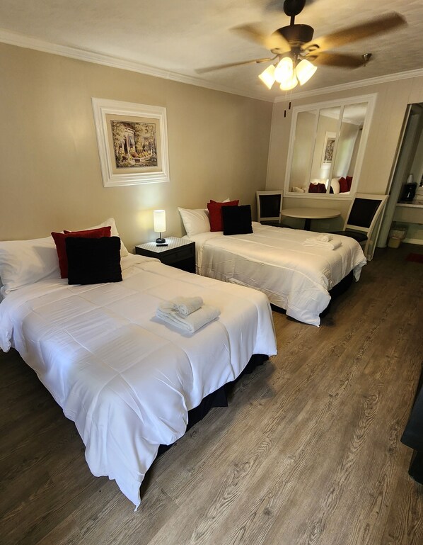 A hotel room with two beds, a round table, a ceiling fan, and a large mirror.