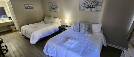 A hotel room with two beds, a ceiling fan, artwork on the walls, a bedside table with a lamp, and a window with a view.