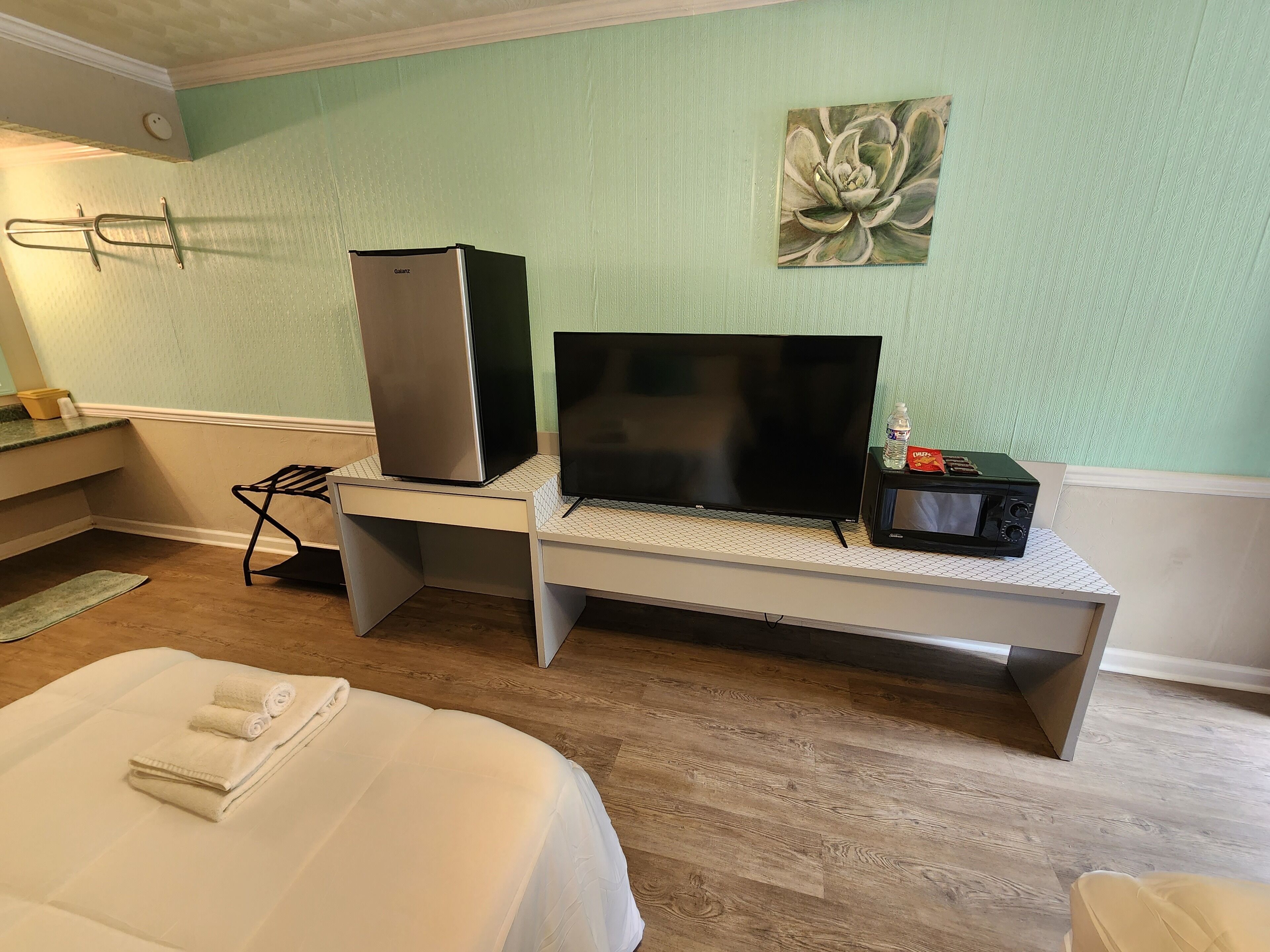A hotel room with a bed, a desk with a refrigerator, a flat-screen TV, and a microwave.