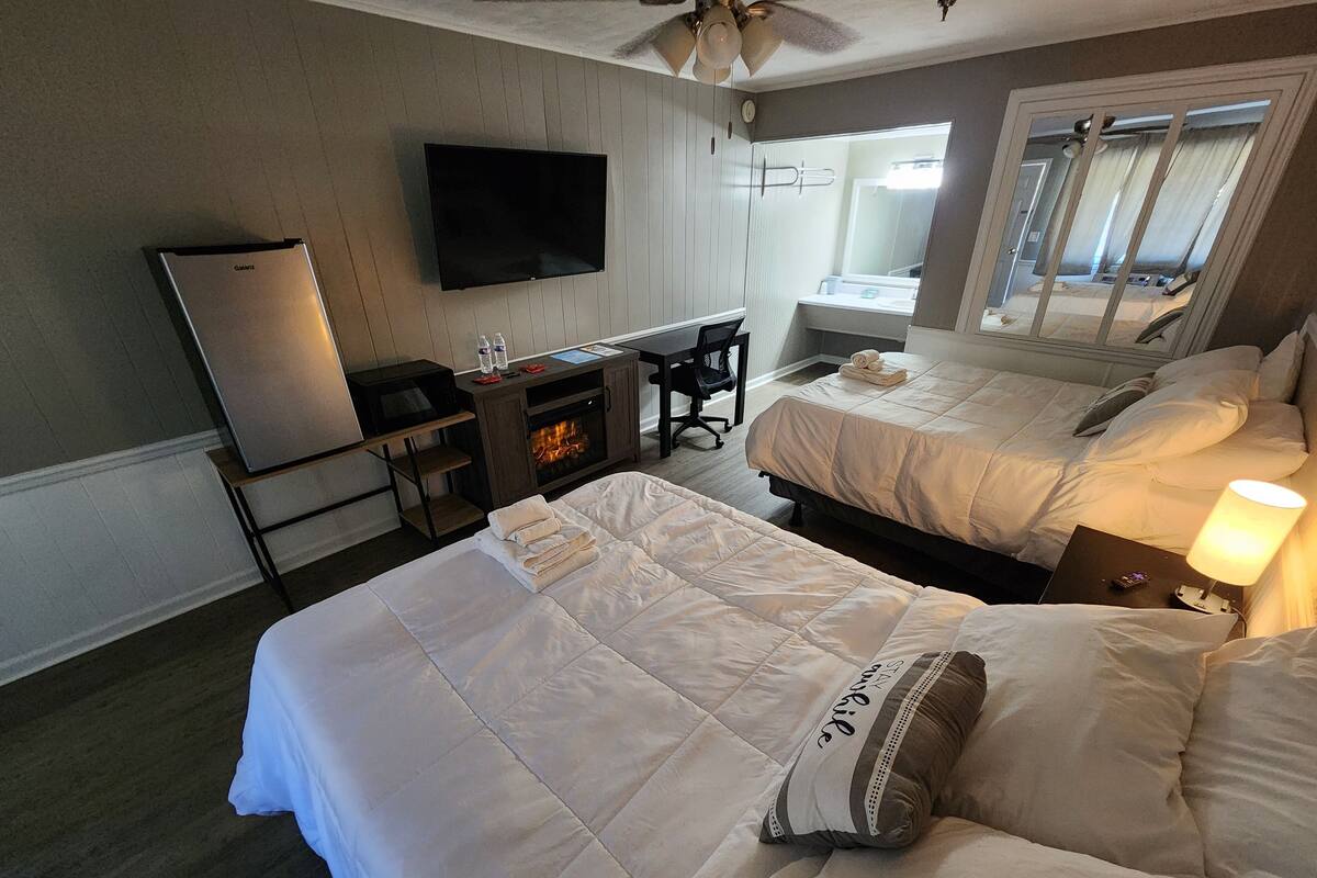 Een hotelkamer met twee bedden, een bureau, een flatscreen-tv en een open haard.