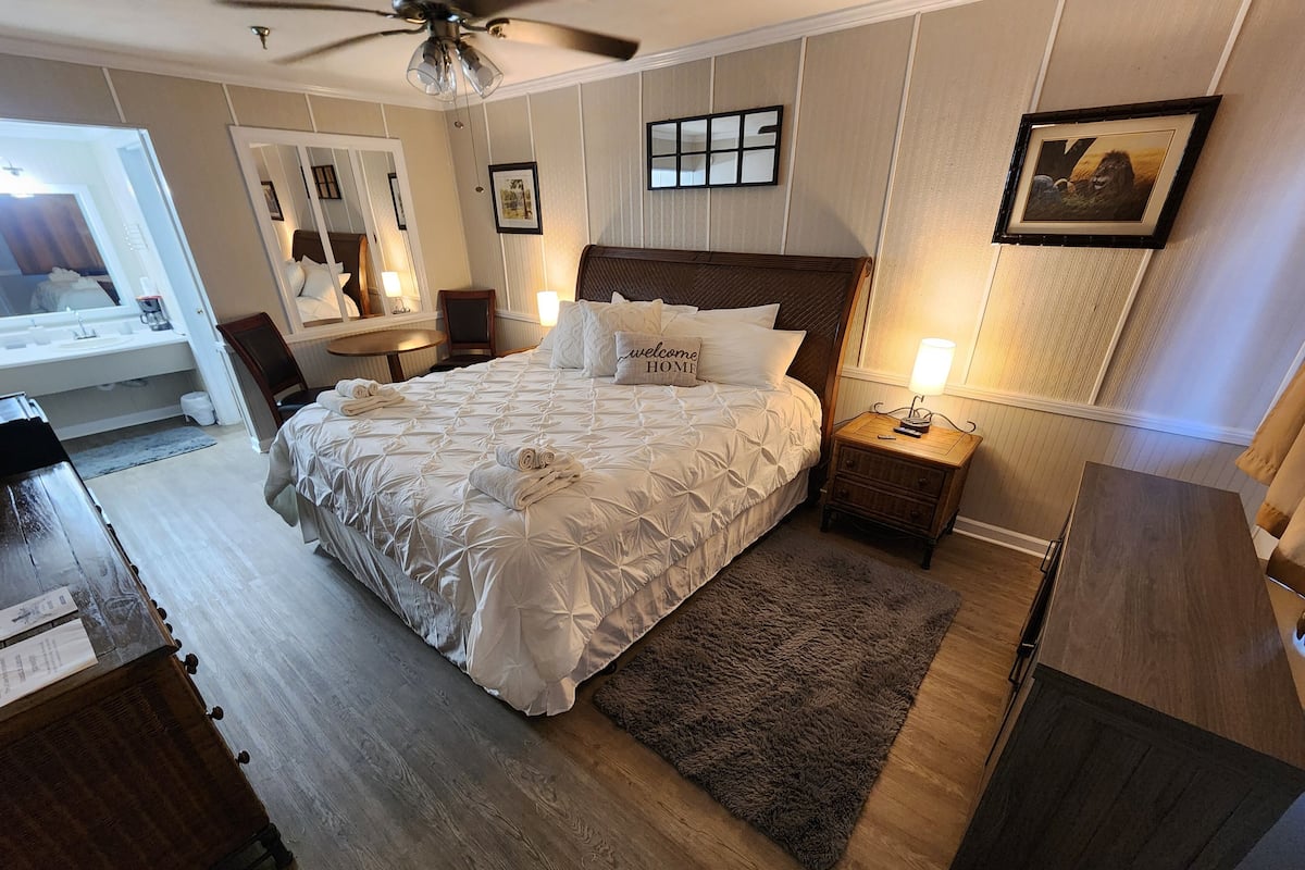 Een stijlvol ingerichte slaapkamer met een groot bed, een houten nachtkastje, een zacht tapijt en een plafondventilator.