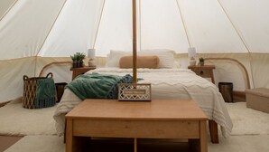 A tented room with a bed, a wooden bench, and a small table with a lamp. - Cozy campsite with creek access! (Landisburg)