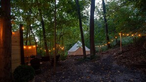 A rustic cabin with a tent and string lights in a forest setting. - Cozy campsite with creek access! (Landisburg)